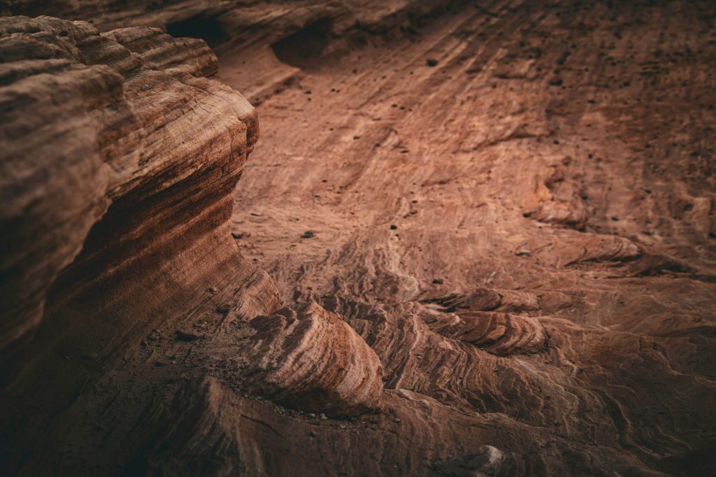 Close-up of reddish sandstone with layered strata and weathered grooves forming natural curves and ridges in a canyon landscape.